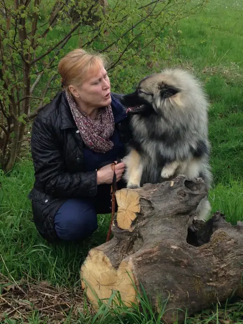 Renate hockt im Garten an einem Baumstamm und schmust mit einem Wolfsspitz